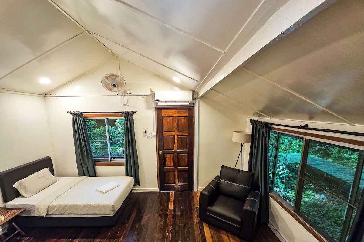 Une chambre à coucher avec un lit, une chaise, une fenêtre donnant sur un paysage verdoyant et un ventilateur de plafond.