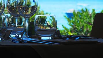 Un tavolo apparecchiato con bicchieri da vino e un bicchiere d'acqua, con vista su spazi verdi e il mare sullo sfondo.