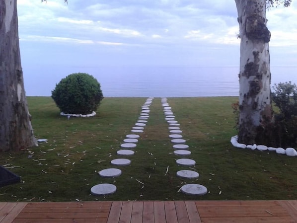 Una terraza de madera que conduce a un sendero circular de piedra con vista al mar.