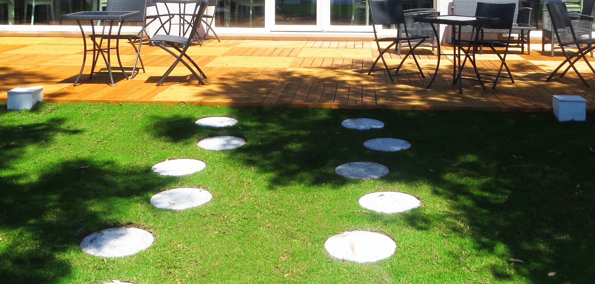 Una zona patio con un pavimento in legno, arredi da esterno e un prato con sentieri in pietra.