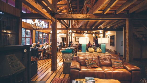 Un interior acogedor con techo de madera, sofá de cuero y una zona de comedor con mesas y sillas.