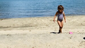 Niño en una playa arenosa, con un lago y montañas al fondo.