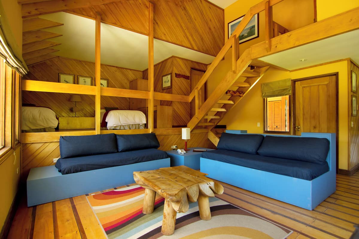 Interior acollidor d'una cabana amb una escala de fusta, un sofà blau i una taula de cafè de fusta.