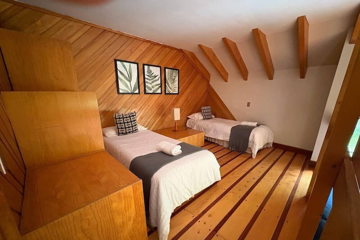 Habitació amb dos llits, terres de fusta i sostre inclinat amb bigues de fusta.