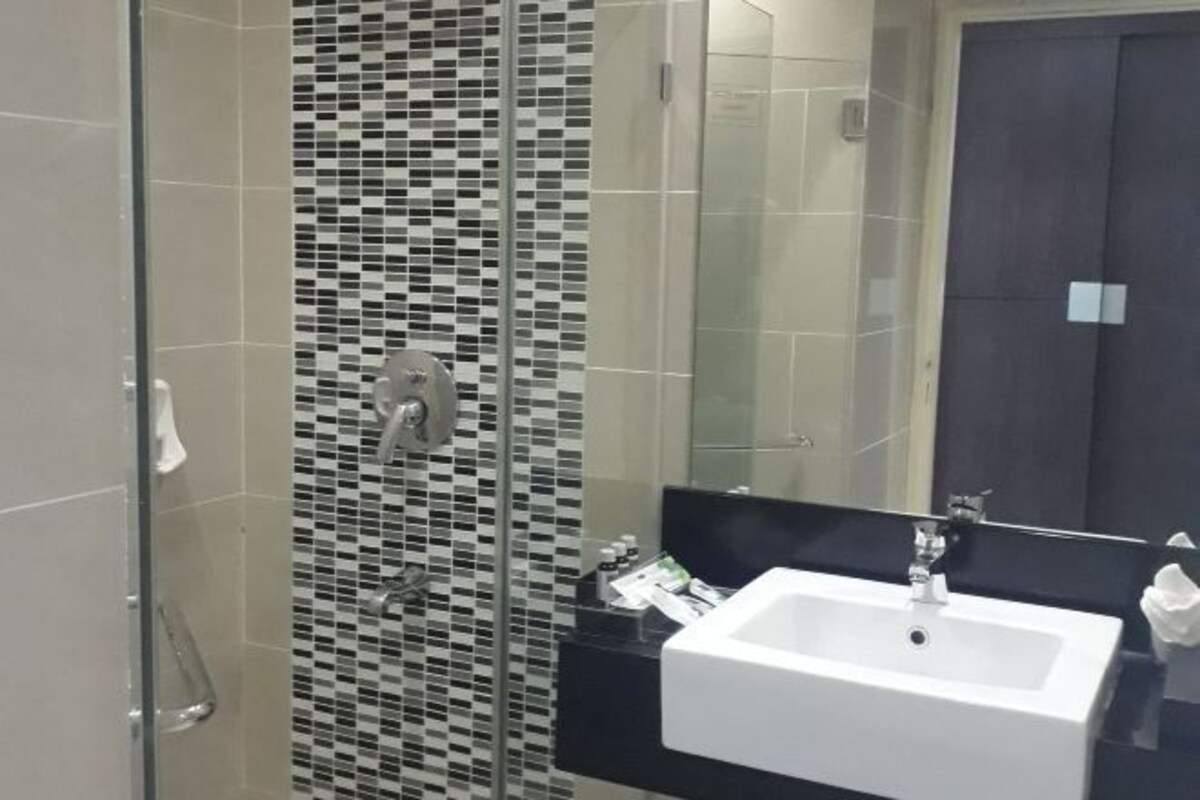 A modern bathroom with a glass shower enclosure, a black countertop, and a white sink.