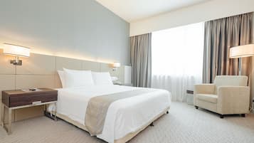A hotel room with a large bed, bedside tables, a chair, and a window with curtains.