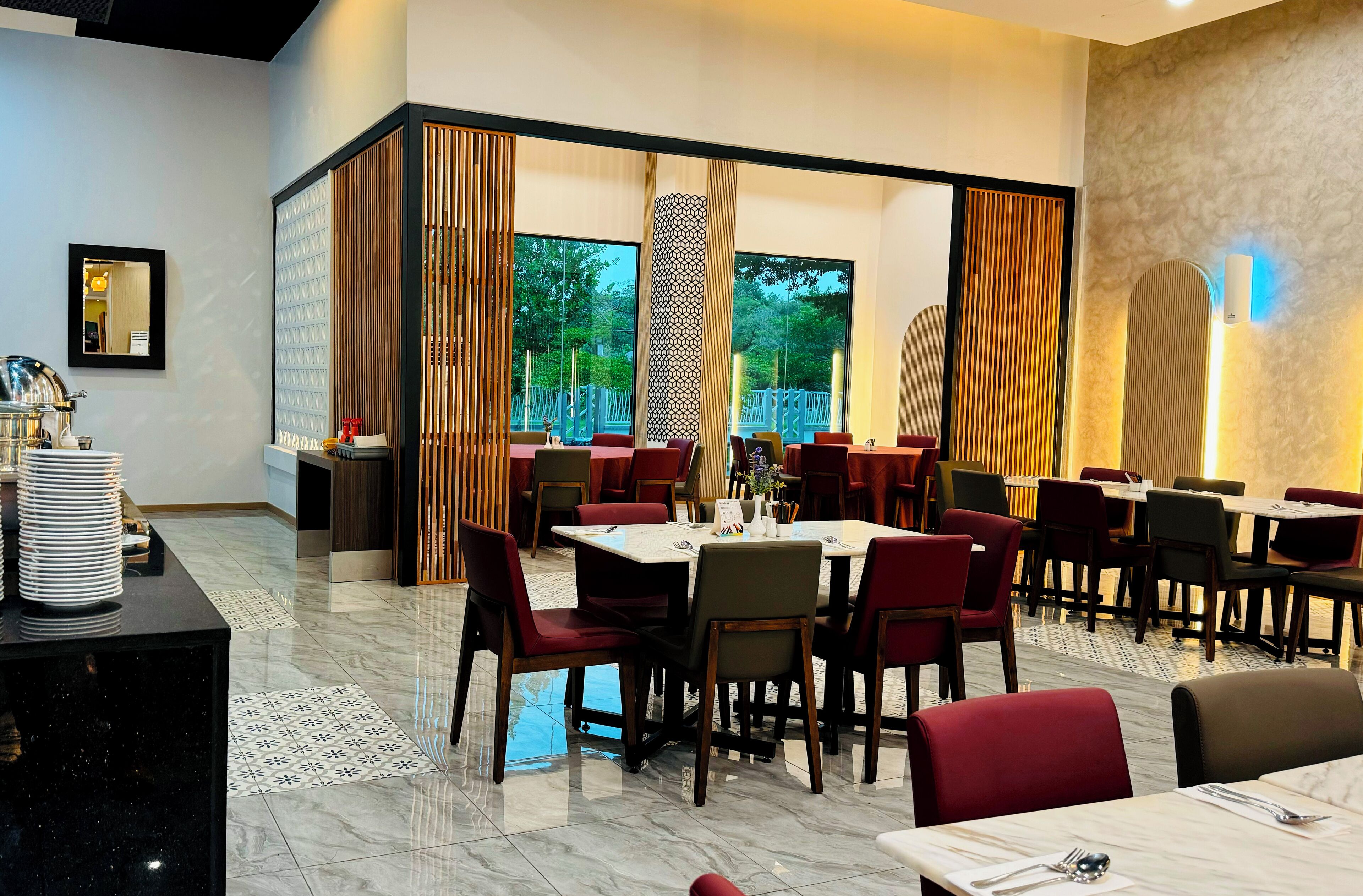 Un restaurante con varias mesas y sillas, ventanas amplias y una pared decorativa.