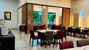 Un restaurante con varias mesas y sillas, ventanas amplias y una pared decorativa.