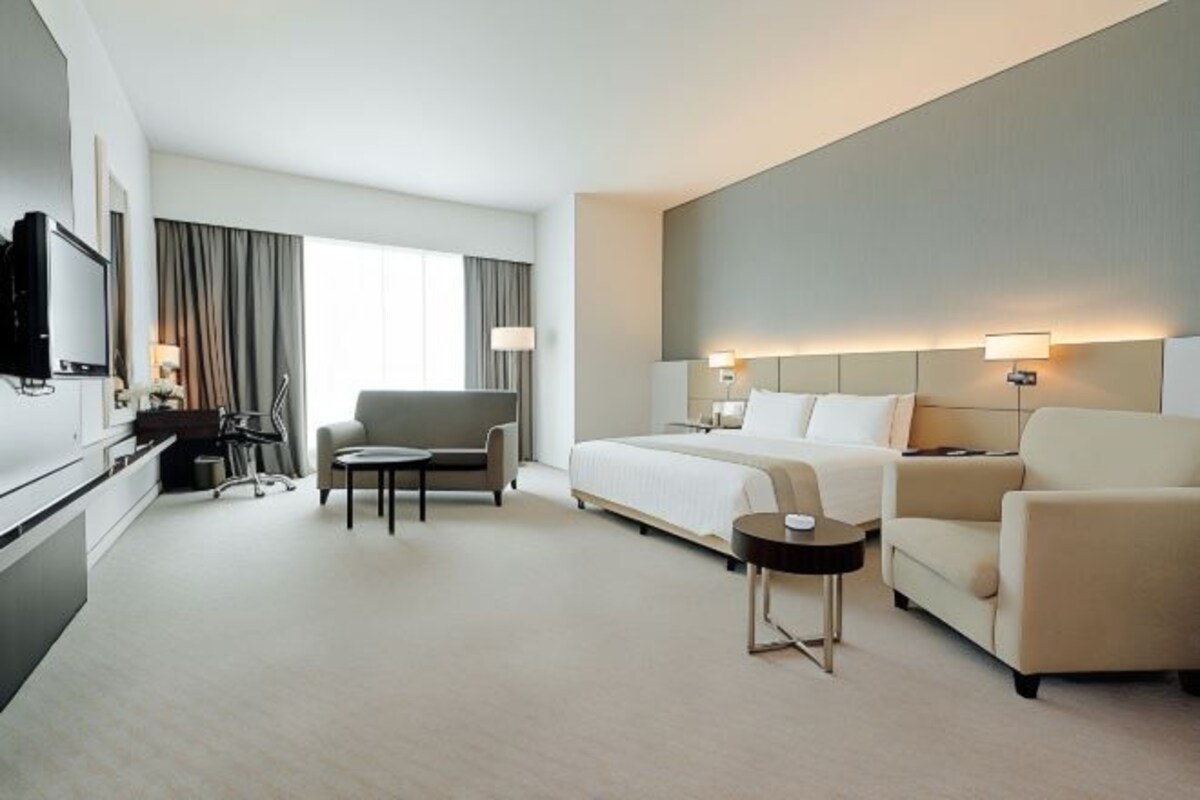 A modern hotel room with a bed, two armchairs, a sofa, a desk, and a television.