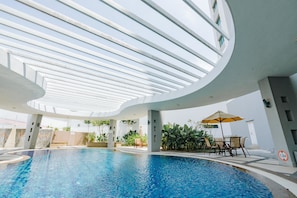 A modern indoor swimming pool with a curved ceiling and skylights, surrounded by lounge chairs and potted plants.