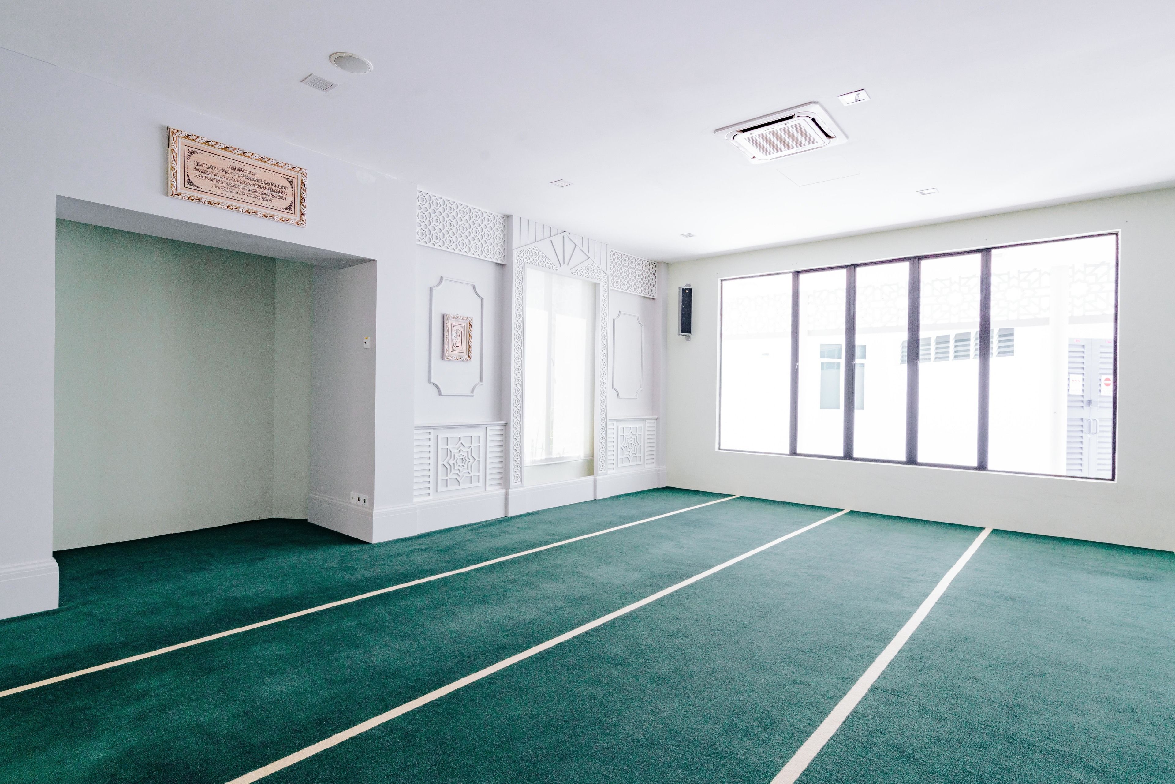 A spacious room with a green carpet, white walls, and large windows.