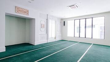 A spacious room with a green carpet, white walls, and large windows.