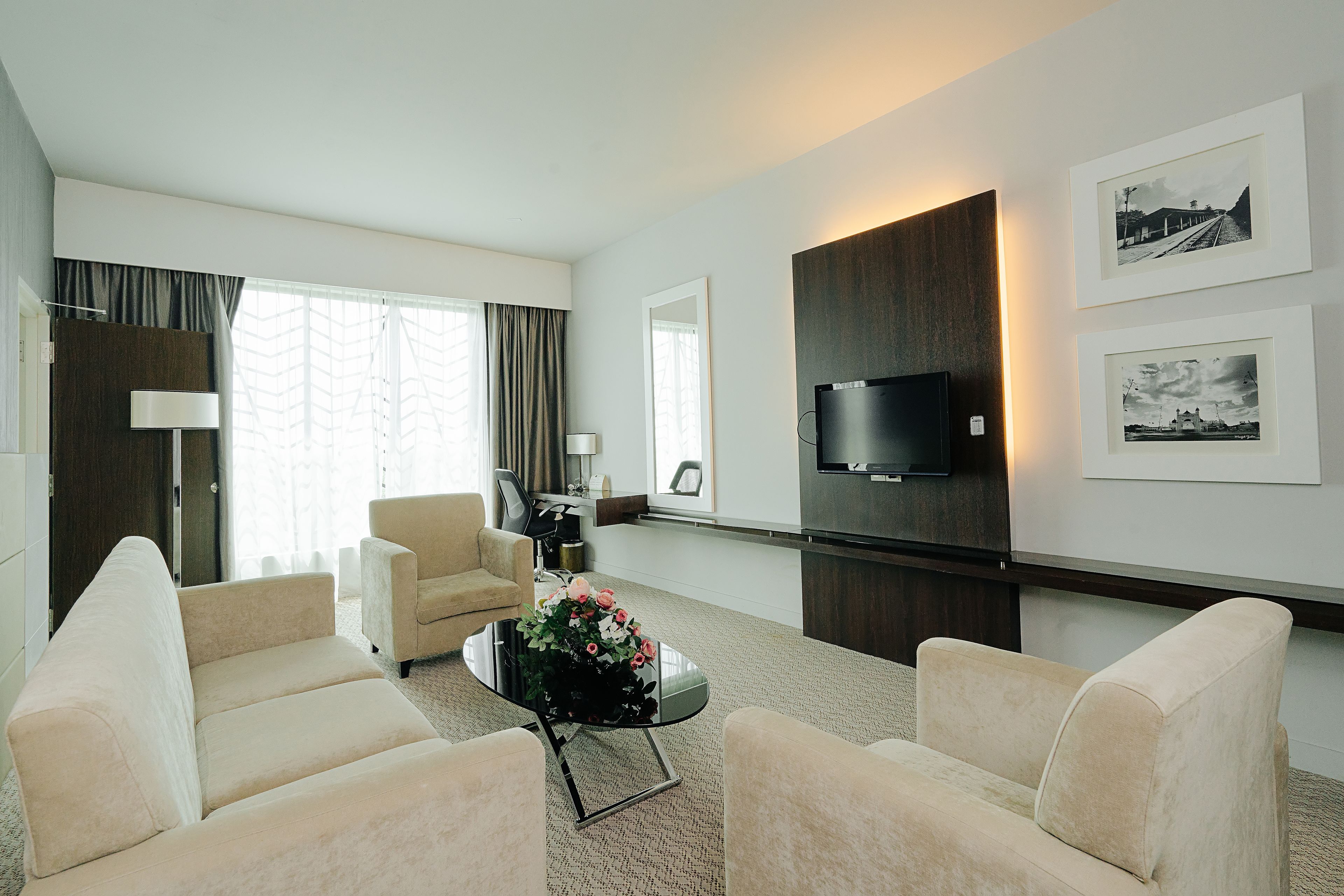 A modern living room with a sofa, armchairs, a coffee table with flowers, a flat-screen TV, and framed pictures on the wall.