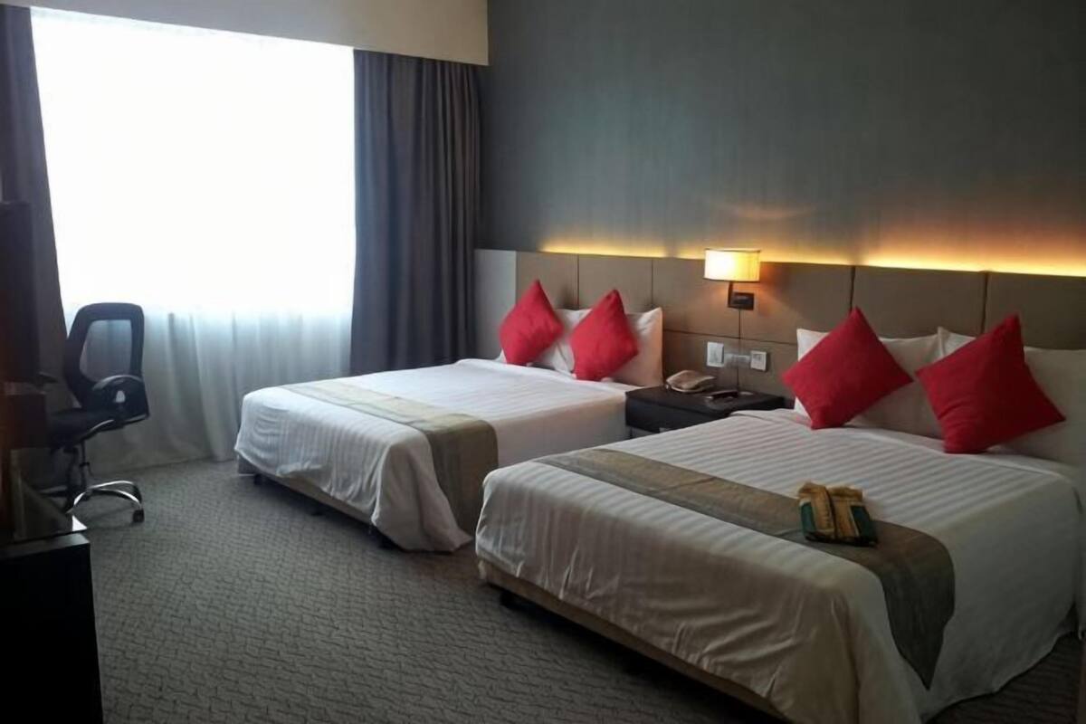 Quarto de hotel com duas camas, uma escrivaninha, uma cadeira e uma janela com cortinas.