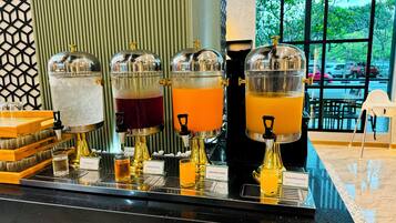 Una estación de bebidas con cuatro dispensadores etiquetados como agua con hielo, jugo de manzana, jugo de naranja y jugo de piña.