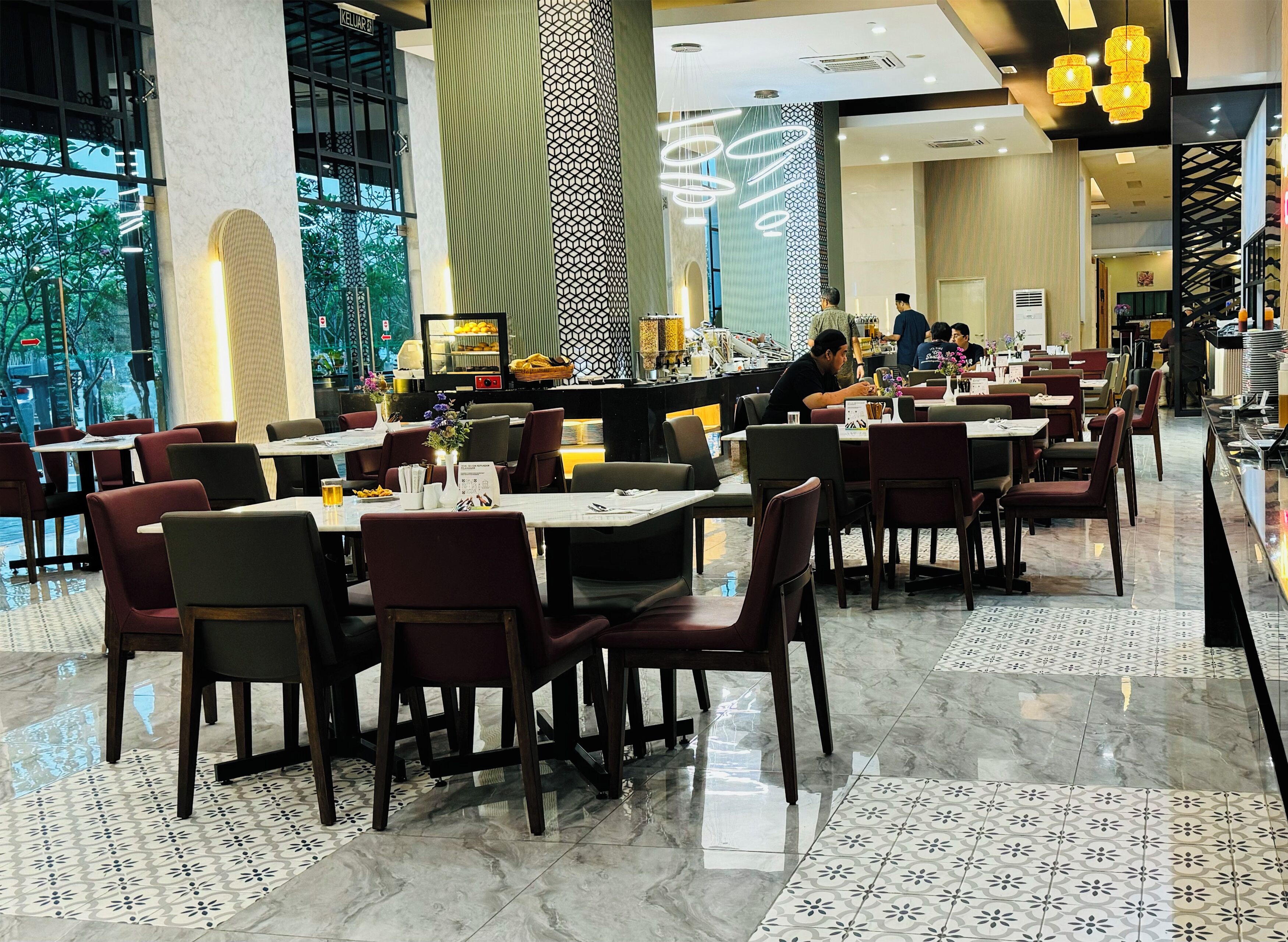 A modern restaurant with multiple dining tables and chairs, a patterned floor, and a view of the outdoors.