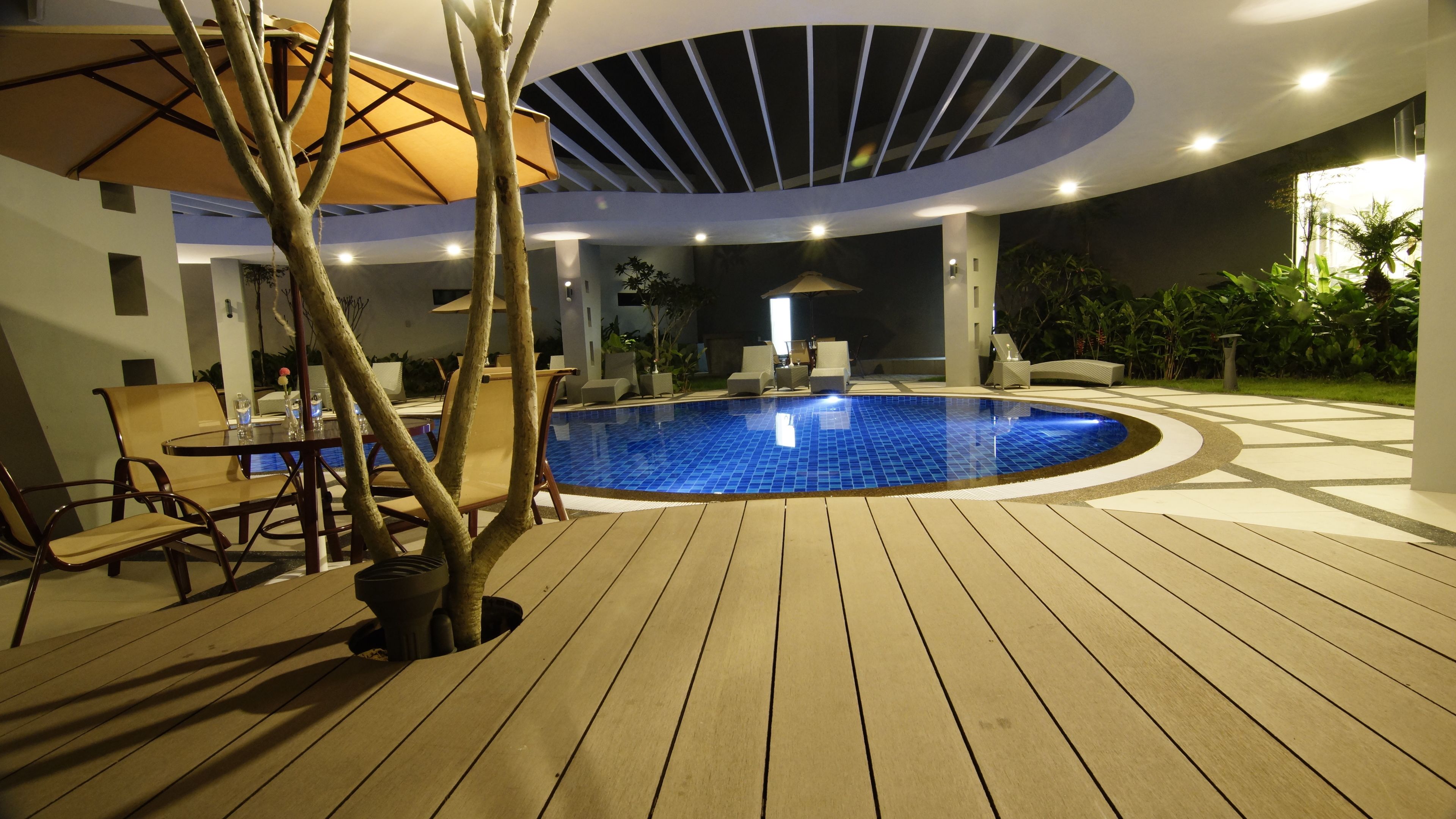 A swimming pool with a wooden deck, surrounded by lounge chairs and a covered seating area.