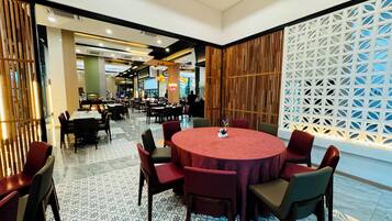 A spacious dining area with round tables and chairs, a patterned floor, and a decorative wall with a geometric design.