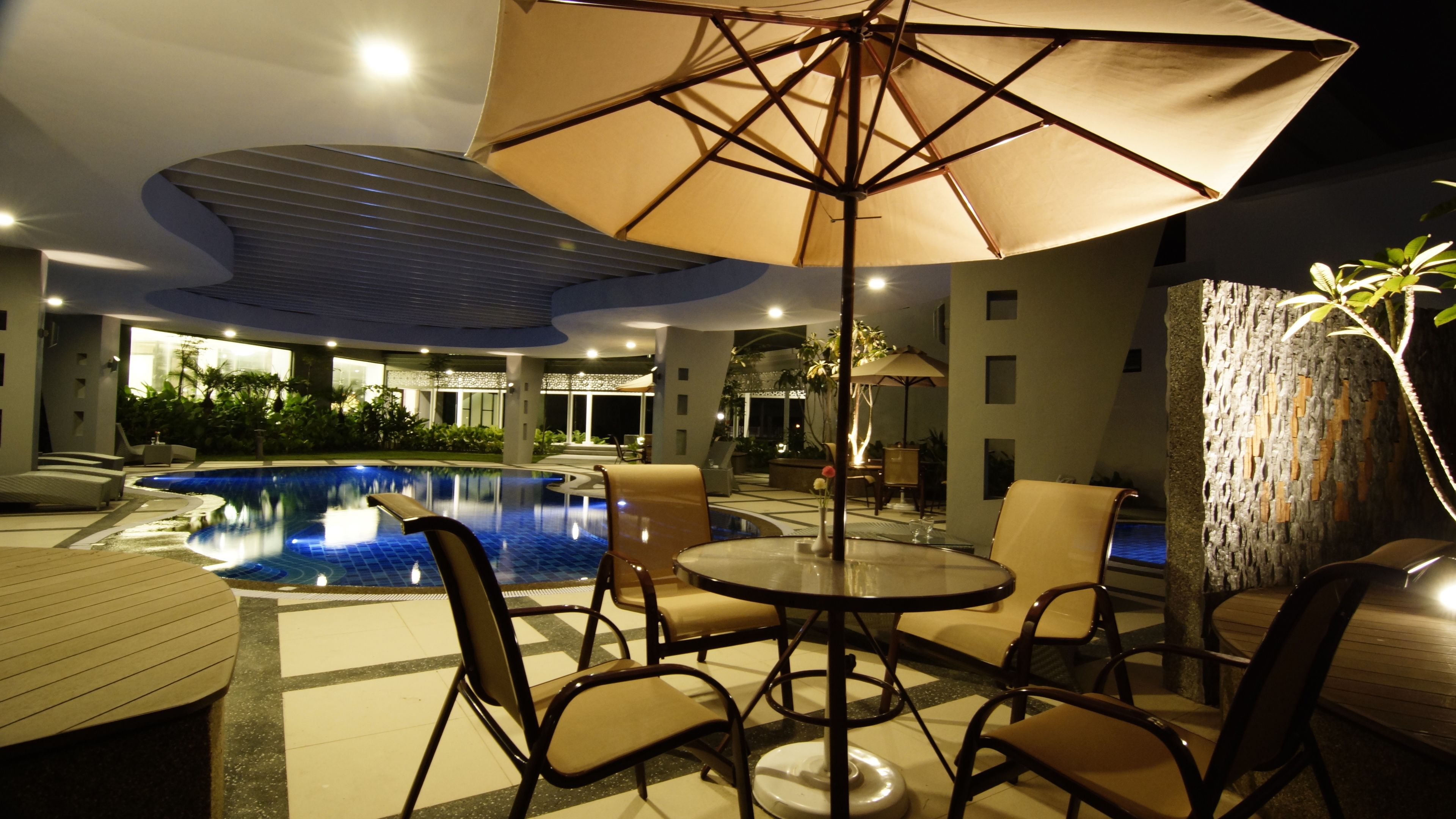 A poolside area with a table and chairs, a large umbrella, and a view of the pool.