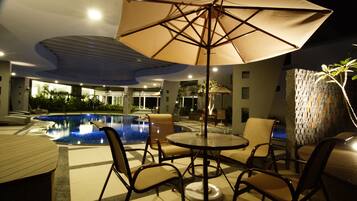 A poolside area with a table and chairs, a large umbrella, and a view of the pool.