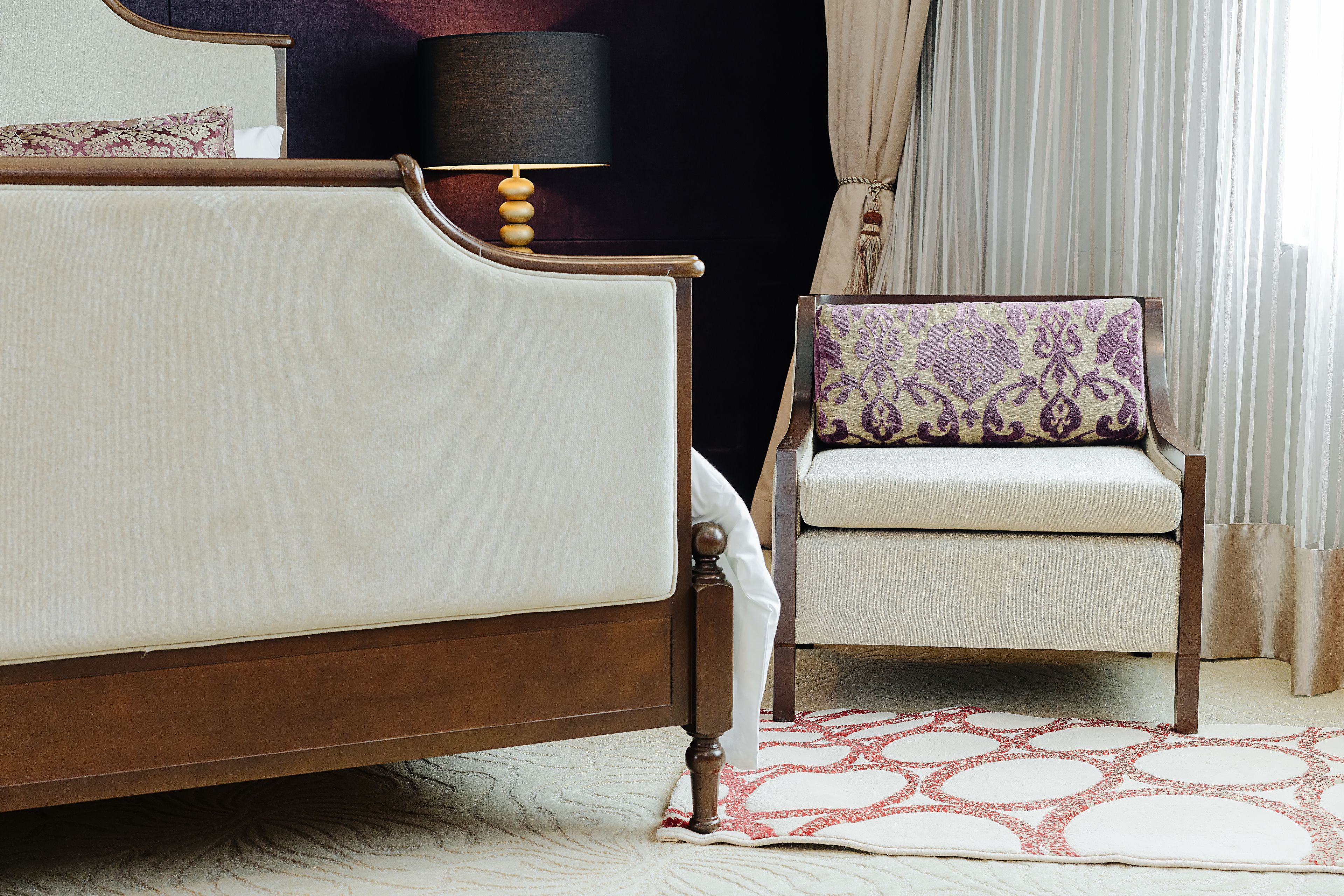 A bedroom with a bed, a chair, a lamp, and a patterned rug.