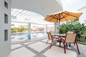 Un área de piscina con techo de cristal, una mesa con sillas y una sombrilla.