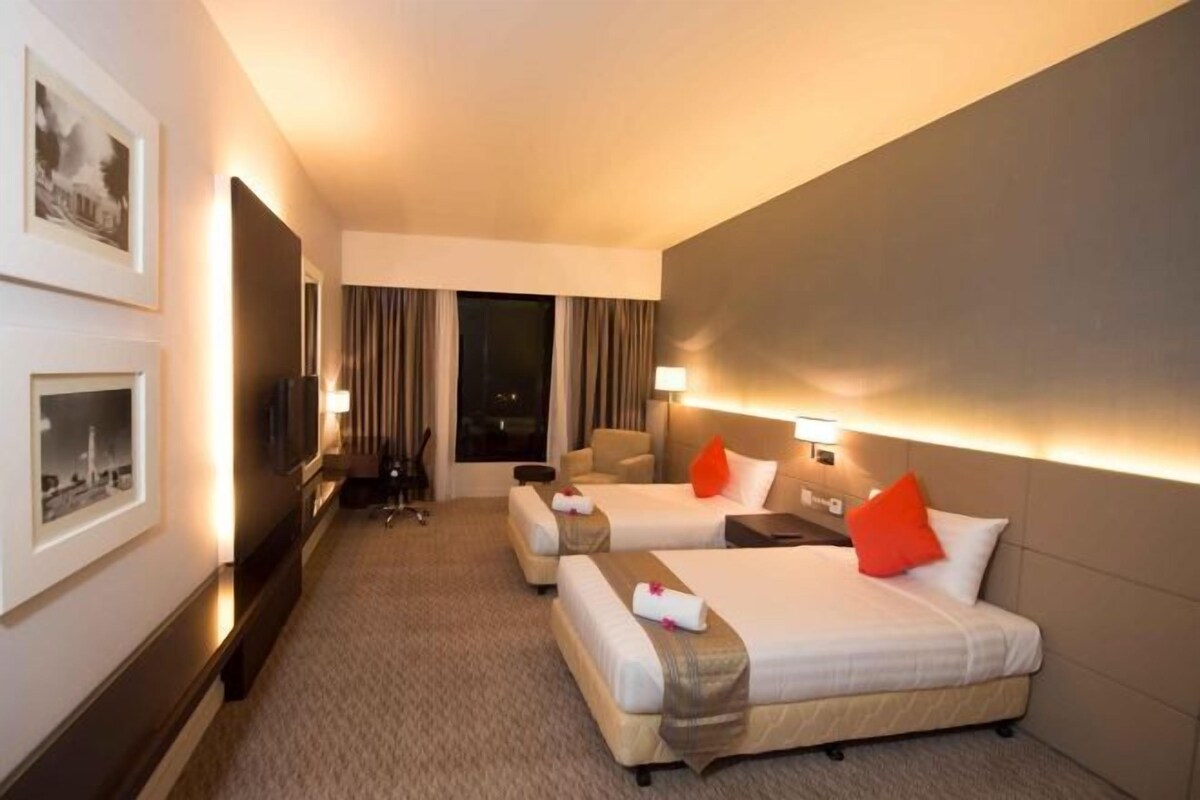 A hotel room with two beds, a desk, a chair, a TV, and framed pictures on the wall.