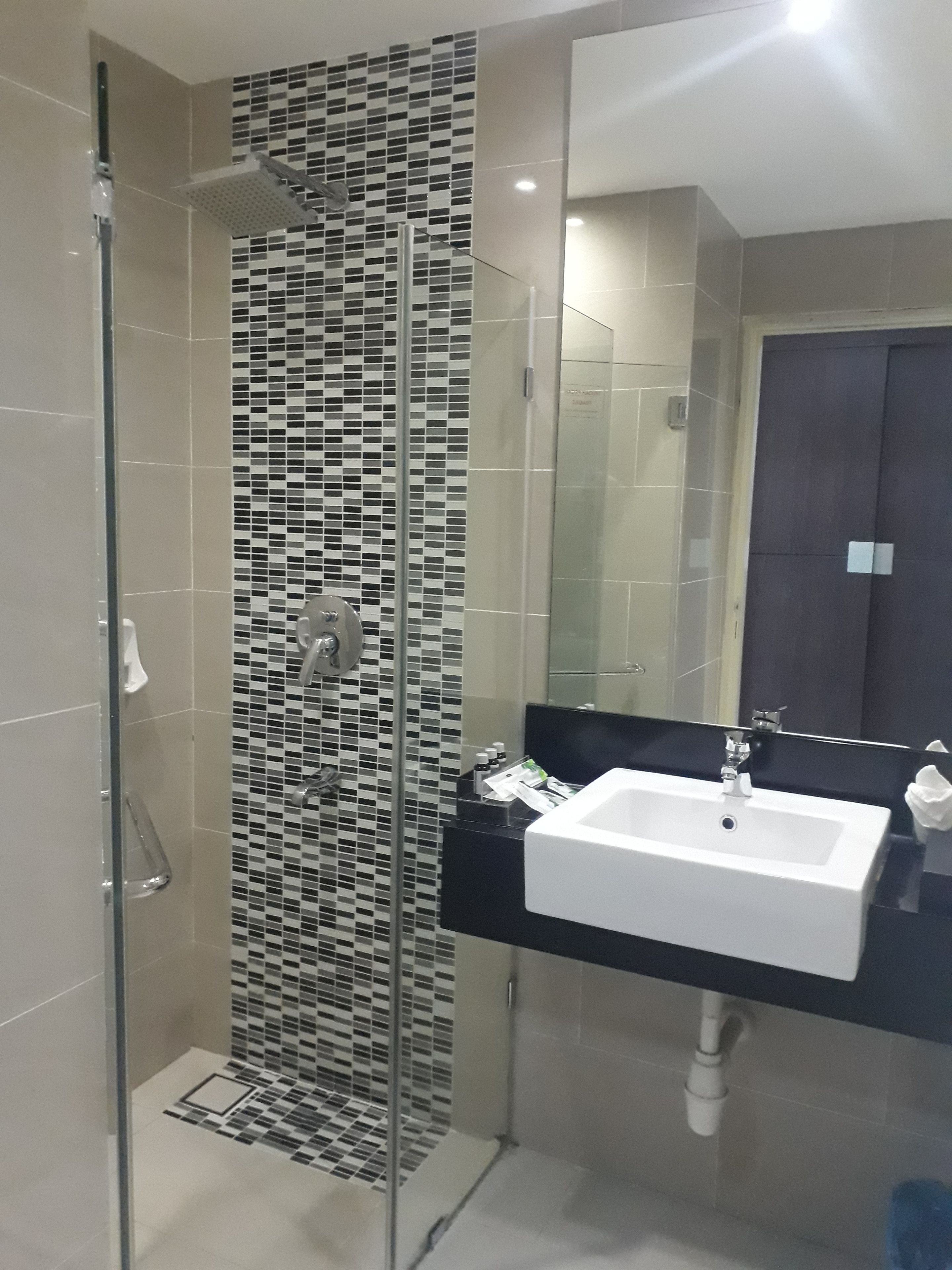Een moderne badkamer met een glazen douchecabine, een betegelde mozaïekwand, een witte wastafel en een donker aanrecht.