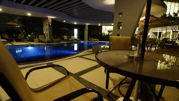 Una piscina interior con sillones de descanso y una mesa, rodeada de paredes e iluminación en el techo.