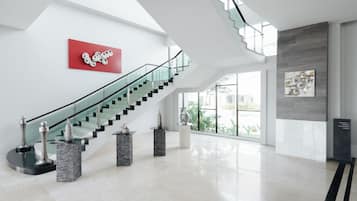 Een ruime lobby met een glazen trap, moderne kunstwerken en een helder uitzicht op het buiten.