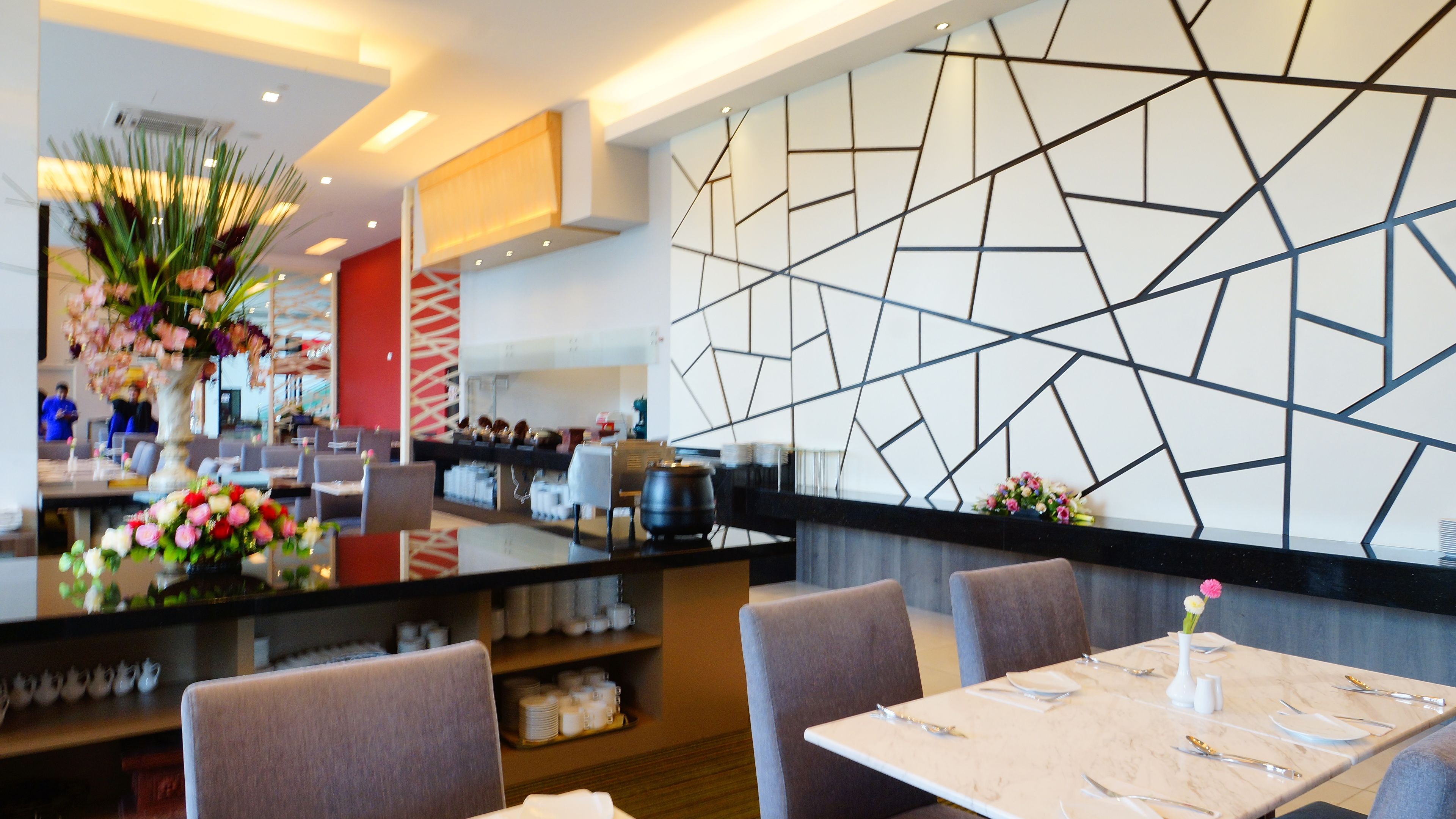 Un restaurante moderno con un diseño geométrico en la pared, mesas de mármol y diversas opciones de asientos.