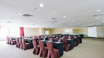 Une salle de conférence équipée de plusieurs tables et chaises, d’un écran de projection et d’un sol recouvert de moquette.