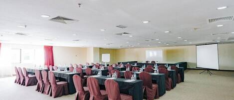 A conference room with multiple tables and chairs, a projector screen, and a carpeted floor.