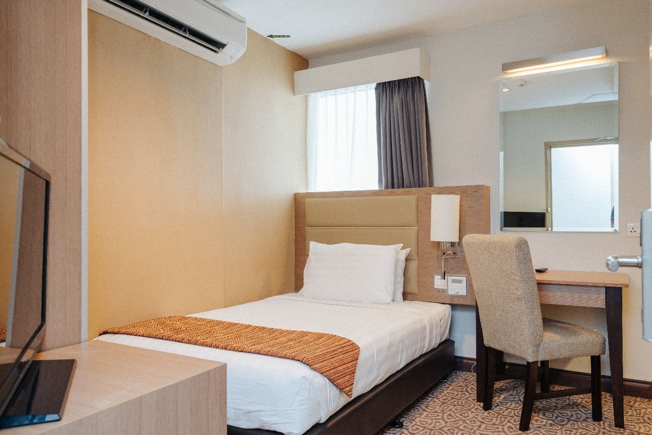 Habitación de hotel con cama, escritorio, silla, espejo y unidad de aire acondicionado.