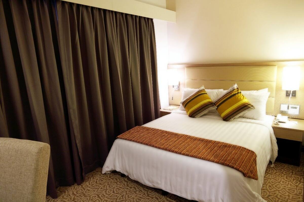 Une chambre d’hôtel avec un grand lit, une table de chevet, une lampe et un rideau.