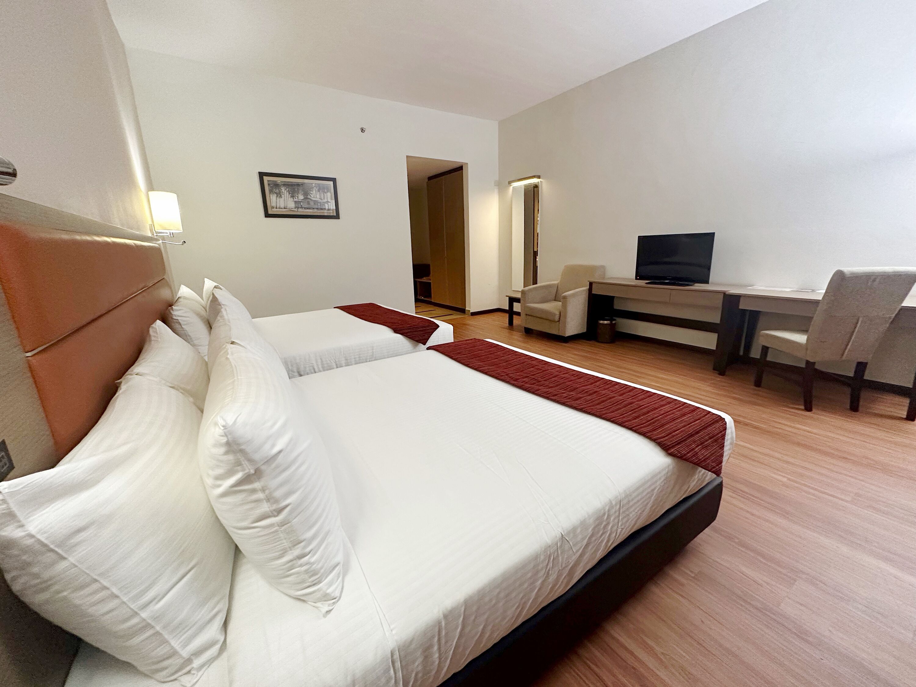 A hotel room with two beds, a desk with a chair, a television, and a framed picture on the wall.