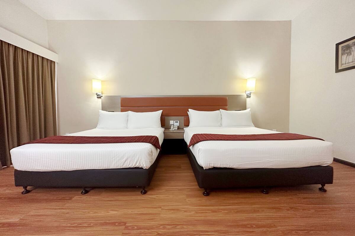 Une chambre d’hôtel avec deux lits, un plancher en bois et une tête de lit dotée de lampes fixées au mur.