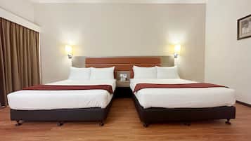 A hotel room with two beds, wooden flooring, and a headboard with wall-mounted lights.