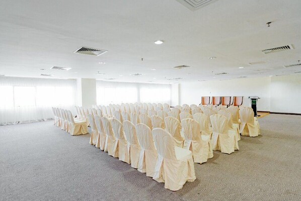 Una sala amplia y bien iluminada con filas de sillas cubiertas con fundas blancas, dispuestas para un evento.