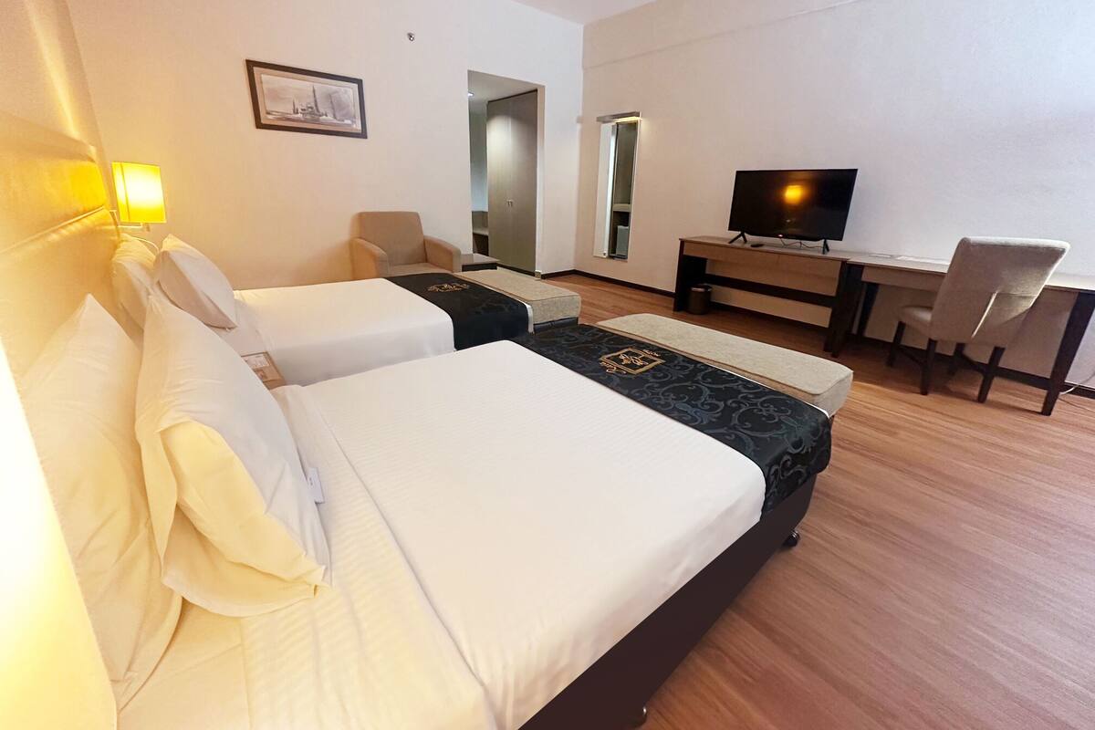 Une chambre d’hôtel avec deux lits, un bureau, une chaise, une télévision et un tableau encadré au mur.