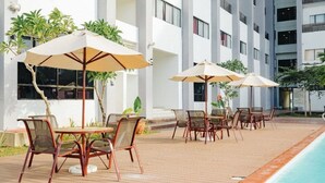 A poolside area with outdoor seating and umbrellas, surrounded by a multi-story building with balconies. - Raia Hotel & Convention Centre Terengganu (Kuala Terengganu)