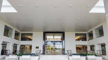 A spacious lobby with a high ceiling, large windows, and a central staircase.