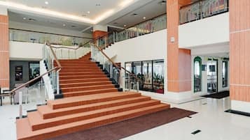 A spacious indoor area with a central staircase leading to an upper level, surrounded by glass railings and modern architectural elements.