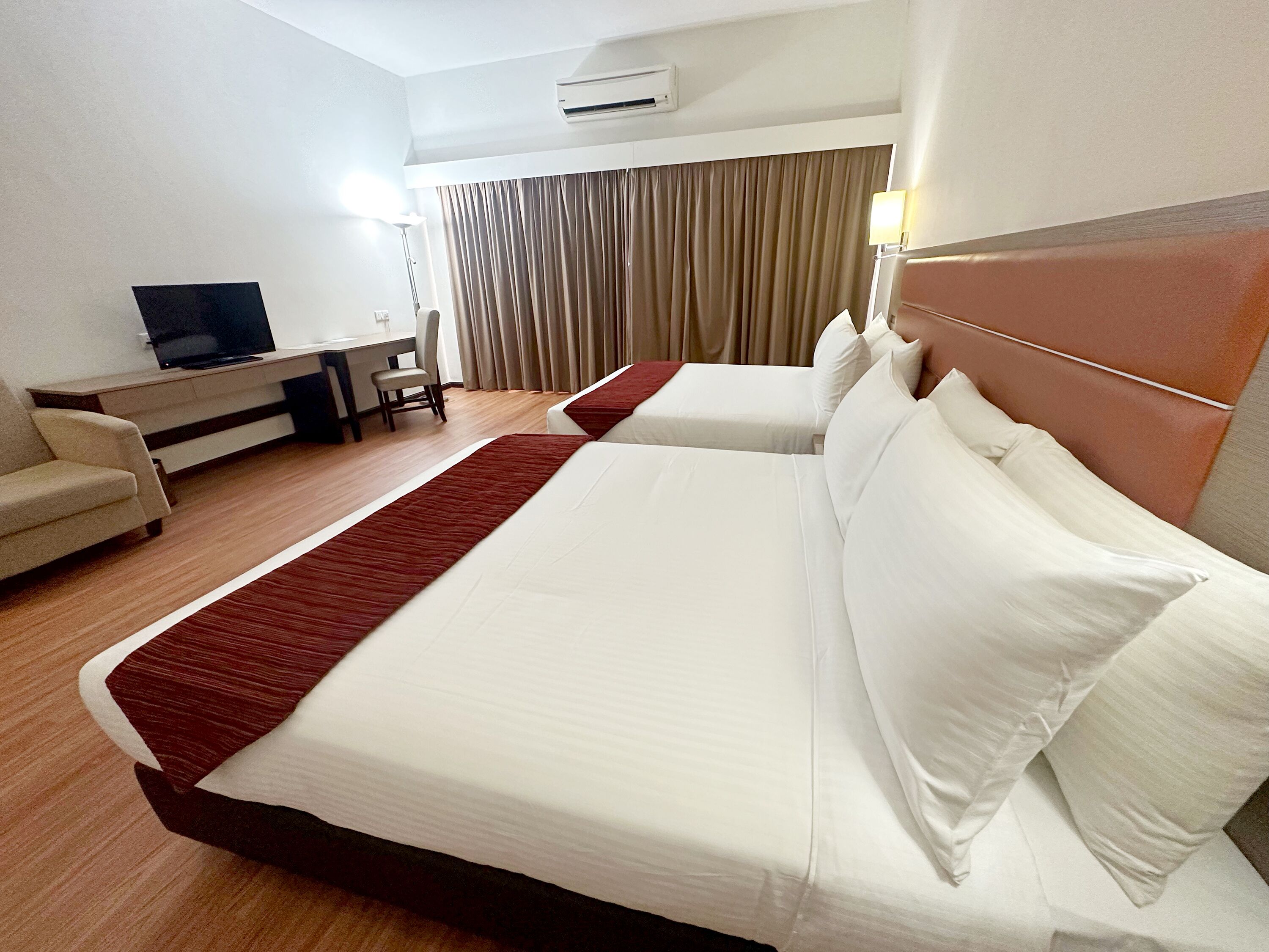 Habitación de hotel con dos camas, un escritorio, una silla y un televisor.