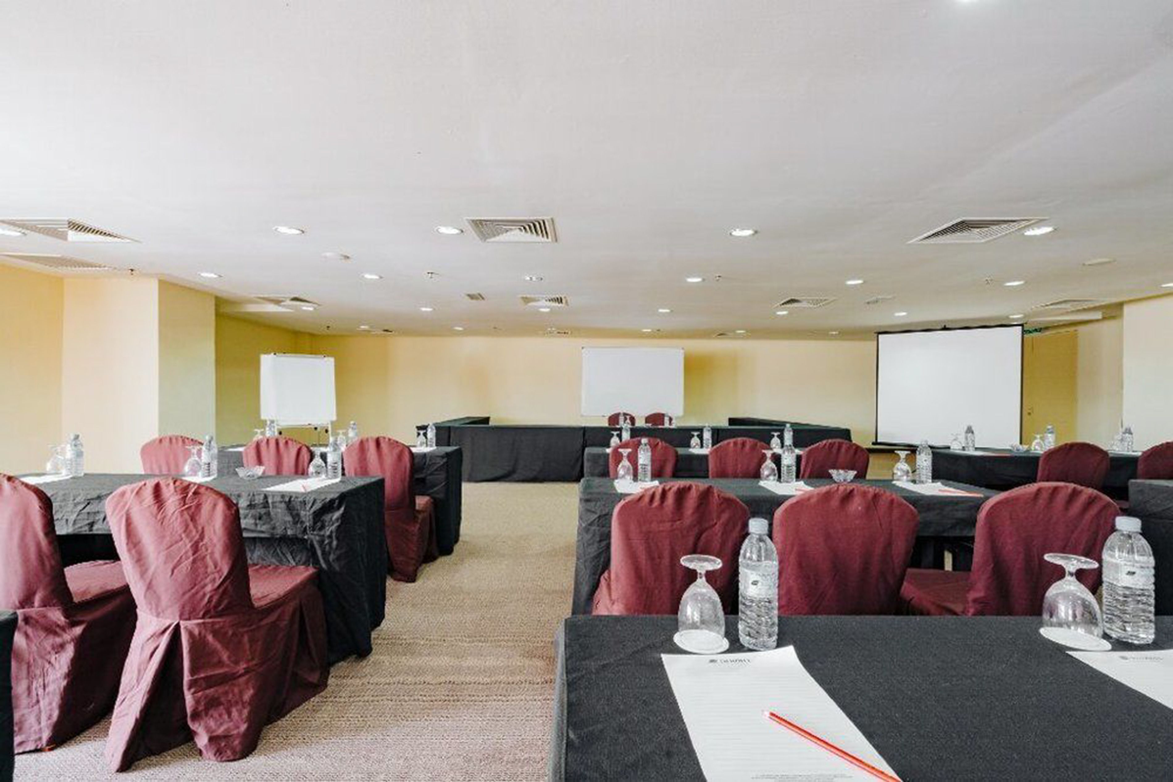 Una sala de conferencias con mesas, sillas y una pantalla de proyector.