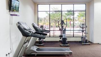 Une salle de sport équipée de tapis de course, de vélos elliptiques et d’un téléviseur fixé au mur.