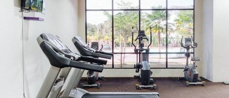 A gym with treadmills, ellipticals, and a television on the wall.