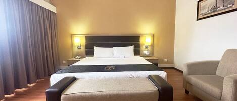 A hotel room with a large bed, bedside lamps, a chair, and a framed picture on the wall.