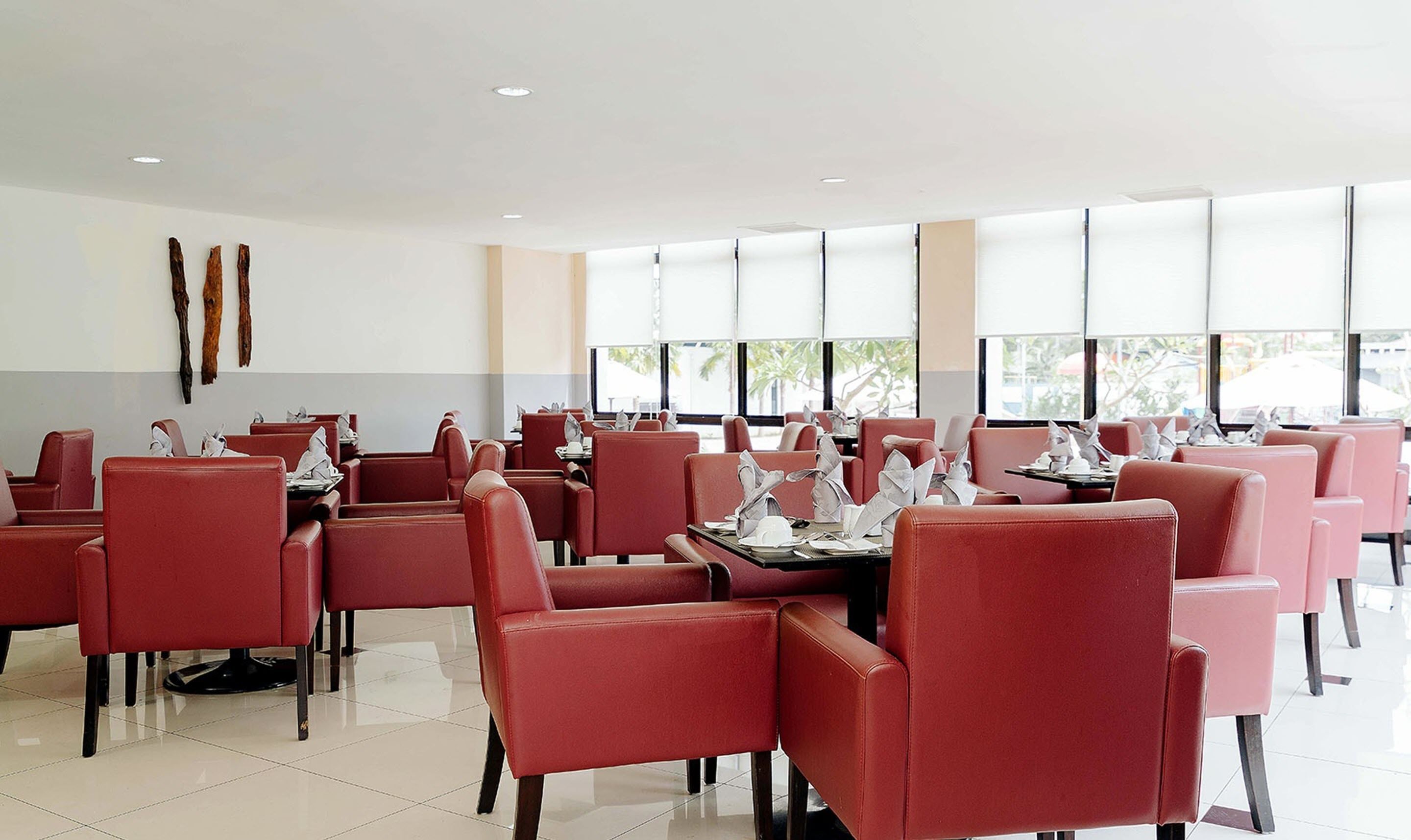 A restaurant with red chairs and tables, large windows, and a tiled floor.