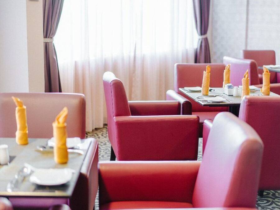 A restaurant with red upholstered booths and tables set with yellow napkins and silverware.